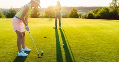female golf player playing golf at golf course with male instructor in background