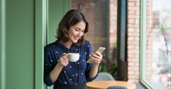 Woman smiling and holding a cup of coffee while looking at phone