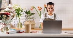Young flower shop owner using laptop on counter while standing.