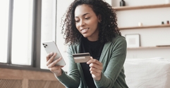 Woman looking at her phone and holding a credit card