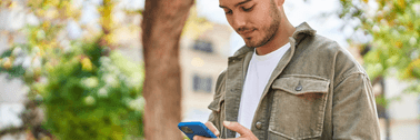A young person looks down at their phone while standing outside.