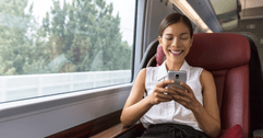 A woman smiles while playing on her phone on a train.