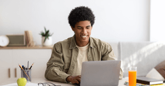 A man smiles while using his laptop at home.