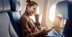 A woman uses her phone and laptop while sitting in an airplane seat.