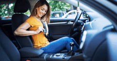 A woman in an orange shirt smiles as she puts on her seatbelt.