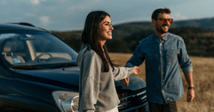 A couple stands in front of their vehicle while enjoying a mountain view.