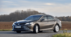 A man drives a dark gray Toyota Camry. 