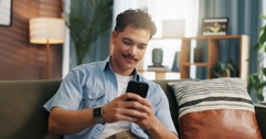 Man playing on phone sitting on couch while smiling slightly