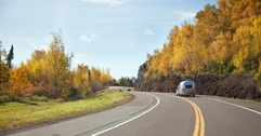 Minnesota road with trees on either side and a car pulling a trailer as the focus