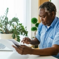 man sitting in his home office with bills in hands