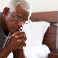 depressed senior man looking unhappy sitting on side of bed
