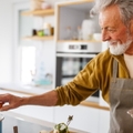 happy senior man cracking eggs and cooking pasta in kitchen