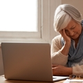 elderly woman sitting in front of her laptop looking stressed