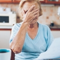 senior woman covering her face in stress while looking at utility bills in kitchen