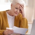 upset senior lady reading bills having financial troubles