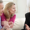senior couple sitting on sofa with male financial advisor discussing documents