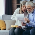 frustrated senior couple sitting on couch at home reviewing bills and taxes