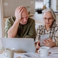 Stressed senior couple calculate expenses or planning budget together while sitting on the table with documents and laptop at home.