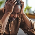 senior african american man sitting at table holding head in stress while looking at notebook