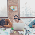 Three coworkers lean over their work table, stressed. 