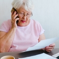 senior woman holding papers while talking on mobile phone