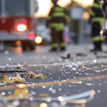 A motorcycle sits next to shattered glass while a firetruck and firefighters are seen in the background.
