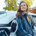 A woman leans against her electric car while it&#x27;s being charged.