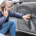 Man looking at car with dent