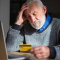 senior man looking worried while holding credit card