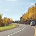 Minnesota road with trees on either side and a car pulling a trailer as the focus