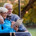 Retired couple on park bench looking at tablet