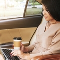 Woman using laptop computer in car while holding a to-go coffee cup