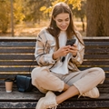Woman sitting on bench using phone while smiling