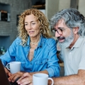 Couple in their 60s sitting at home having coffee and looking at notebook