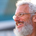 Man with white hair and beard wearing glasses and smiling