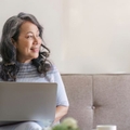 Smiling woman in 60s on couch with laptop