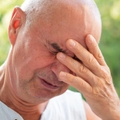 Man in his sixties looking worried with eyes closed and hand on his face