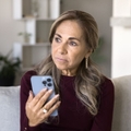 Mature woman holding phone on couch