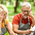 Retired couple sitting outside looking over finances worried faces