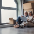 Older couple sitting against moving boxes with laptop