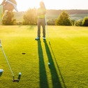 female golf player playing golf at golf course with male instructor in background