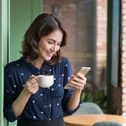 Woman smiling and holding a cup of coffee while looking at phone