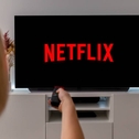 A woman holds up her remote control pointing to her TV, which is showing the Netflix screen.