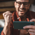 A man cheers while playing a game on his phone.