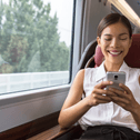 A woman smiles while playing on her phone on a train.