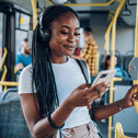 A woman wears headphone and smiles while using her smartphone on a bus.