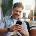 Man playing on phone sitting on couch while smiling slightly