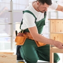 Handyperson wearing overalls assembling wooden furniture