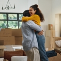 Young couple hugging and celebrating with boxes stacked around them in new house