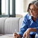 Woman in her fifties at computer writing down notes 